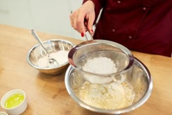 cooking food, baking and people concept - chef with sieve sifting flour into bowl and making batter or dough. chef sifting flour in bowl making batter or dough