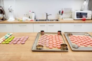 cooking, confectionery and baking concept - macarons on oven trays at bakery or pastry shop kitchen. macarons on oven trays at confectionery