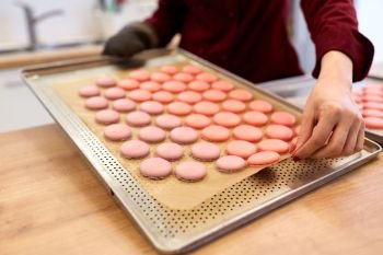 cooking, confectionery and people concept - chef with macarons on oven tray at bakery. chef with macarons on oven tray at confectionery