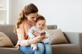 family, technology and motherhood concept - happy smiling young mother with little baby and smartphone at home. happy mother with baby and smartphone at home