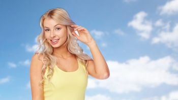 hairstyle and people concept - happy smiling beautiful young woman with blonde hair over blue sky and clouds background. happy smiling young woman with blonde hair