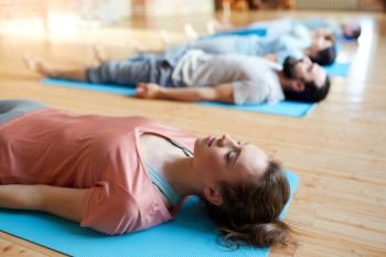 fitness, sport and healthy lifestyle concept - woman with group of people doing yoga corpse pose on mats at studio. woman with group of people doing yoga at studio