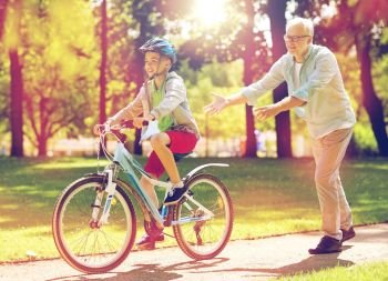 family, generation, safety and people concept - happy grandfather teaching boy how to ride bicycle at summer park. grandfather and boy with bicycle at summer park