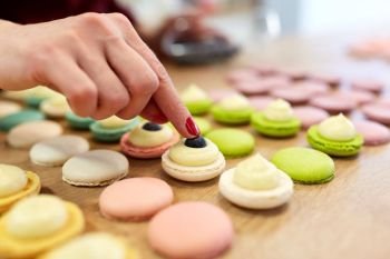 cooking, food and baking concept - chef decorating macarons shells at confectionery or pastry shop. chef decorating macarons shells at pastry shop