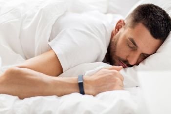 people, bedtime and rest concept - man with smartwatch sleeping in bed. man with smartwatch sleeping in bed