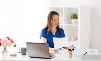business, people and work concept - happy smiling woman with laptop computer working and writing to notebook at office or home. happy woman with papers and laptop at office