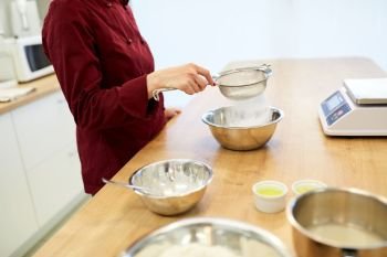 cooking food, baking and people concept - chef with sieve sifting flour into bowl and making batter or dough. chef sifting flour in bowl making batter or dough