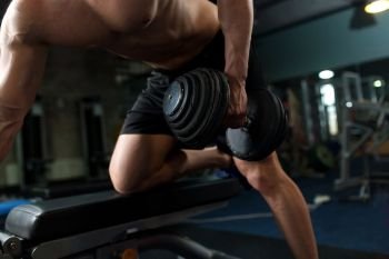 sport, bodybuilding, fitness and people concept - close up of young man with dumbbell and bench flexing muscles in gym. close up of man with dumbbell exercising in gym
