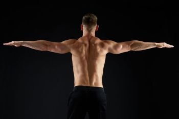 sport, bodybuilding, fitness and people concept - young man or bodybuilder with bare torso over black background from back. young man or bodybuilder with bare torso