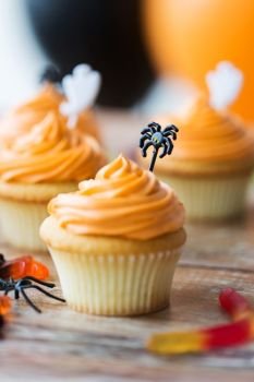 food, baking and holidays concept - cupcakes or muffins and candies with halloween party decorations on wooden table. halloween party cupcakes or muffins on table