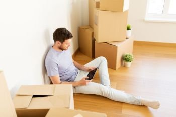 real estate, people and technology concept - young man with tablet pc computer and boxes moving to new home. man with tablet pc and boxes moving to new home
