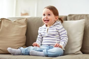 childhood, emotions and people concept - happy smiling baby girl sitting on sofa at home. happy smiling baby girl sitting on sofa at home