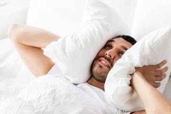 people, bedtime and rest concept - man lying in bed with pillow suffering from noise at home. man in bed with pillow suffering from noise