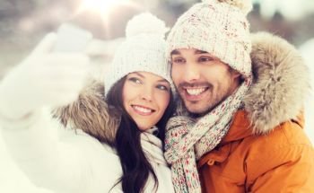 people, season, love, technology and leisure concept - happy couple taking selfie by smartphone over winter background. happy couple taking selfie by smartphone in winter