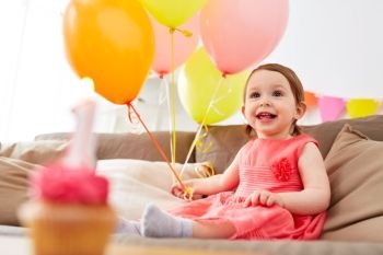 childhood, holidays and people concept - happy baby girl air balloons and garland on birthday party at home. happy baby girl on birthday party at home