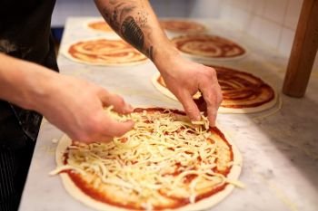 food cooking, culinary and people concept - cook or baker hands adding grated cheese to pizza at pizzeria. cook adding grated cheese to pizza at pizzeria