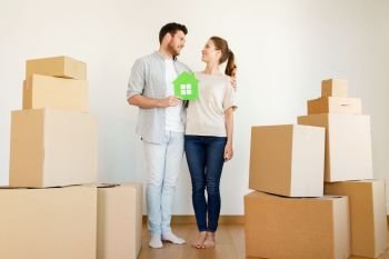 mortgage, people and real estate concept - happy couple with green paper house and boxes moving to new home. happy couple with boxes moving to new home