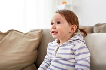 childhood, portrait and people concept - happy smiling baby girl sitting on sofa at home. happy smiling baby girl sitting on sofa at home