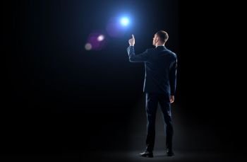 business, technology and people concept - businessman in suit pointing finger to lens flare t over black background. businessman in suit pointing finger to lens flare