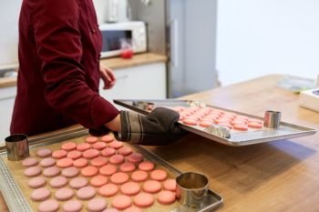 cooking, baking, confectionery and people concept - chef with macarons on oven tray at bakery kitchen. chef with macarons on oven tray at confectionery