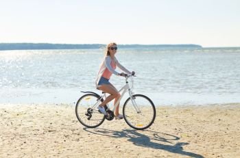 people, leisure and lifestyle concept - happy young woman riding bicycle along summer beach. happy woman riding bicycle along summer beach