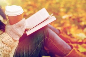 season, technology and people concept - close up of young woman reading book and drinking coffee from paper cup in autumn park. woman with book drinking coffee in autumn park