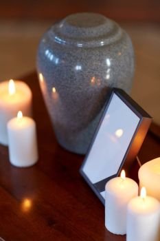 funeral and mourning concept - photo frame with black ribbon, cremation urn and burning candles on table in church. photo frame, cremation urn and candles on table