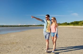 leisure, relationship and people concept - happy couple walking along summer beach and pointing finger to something. happy couple walking along summer beach