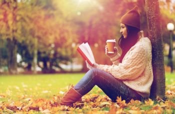 season, literature, education and people concept - young woman reading book and drinking coffee from paper cup in autumn park. woman with book drinking coffee in autumn park