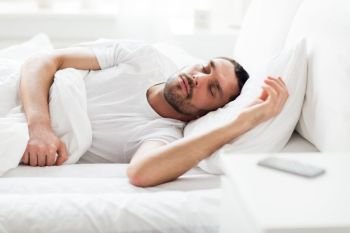 people, bedtime and rest concept - man sleeping in bed at home with smartphone on nightstand. man sleeping in bed with smartphone on nightstand