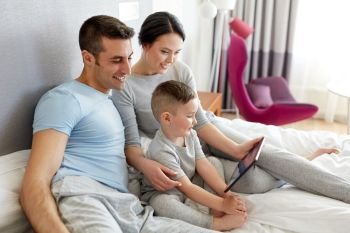 people, family and technology concept - happy mother, father and little boy with tablet pc computer in bed at home or hotel room. happy family with tablet pc in bed at home