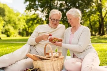 old age, leisure and people concept - happy senior couple with picnic basket eating strawberries at summer park. senior couple with strawberries at picnic in park