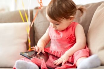 childhood, people and technology concept - happy baby girl with tablet pc computer sitting on sofa at home. baby girl with tablet pc sitting on sofa at home