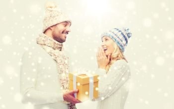 winter, holidays, couple, christmas and people concept - smiling man and woman in hats and scarf with gift box. smiling couple in winter clothes with gift box