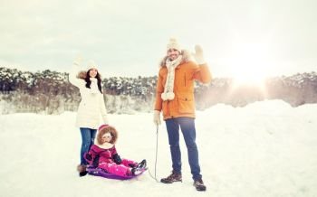 parenthood, fashion, season, gesture and people concept - happy family with child on sled walking and waving hand in winter outdoors. happy family with sled walking in winter outdoors