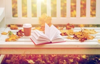 season, education and literature concept - open book and coffee cup on bench in autumn park. open book and coffee cup on bench in autumn park