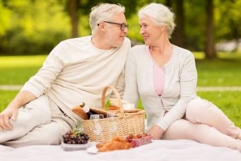 old age, holidays, leisure and people concept - happy senior couple with picnic basket sitting on blanket at summer park. happy senior couple having picnic at summer park