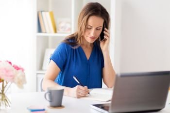 technology, communication and people concept - happy woman calling on smartphone and writing to notebook at office or home. woman with notepad calling on smartphone at office