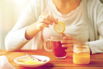 health, traditional medicine and ethnoscience concept - close up of ill woman drinking tea with lemon, honey and ginger at wooden table. close up of ill woman drinking tea with lemon