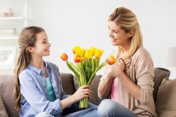 people, family and holidays concept - happy girl giving tulip flowers and kissing her mother at home. happy girl giving flowers to mother at home