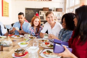 leisure, payment and people concept - happy friends with money paying for food at restaurant. happy friends with money paying at restaurant