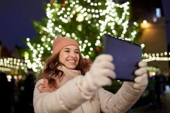 winter holidays and people concept - happy woman with tablet pc taking selfie at christmas tree outdoors. woman with tablet pc at christmas tree outdoors