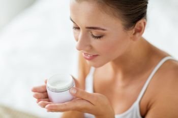 beauty, cosmetics, skin care and people concept - close up of beautiful happy woman holding and smelling cream jar. close up of happy woman holding and smelling cream