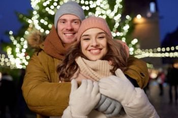 winter holidays and people concept - happy young couple dating and hugging at christmas tree in evening. happy couple hugging at christmas tree
