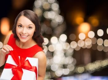 christmas, holidays and people concept - smiling woman in red dress with gift box over lights background. smiling woman in red dress with christmas gift box