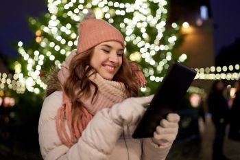 winter holidays and people concept - happy woman with tablet pc at christmas tree outdoors. woman with tablet pc at christmas tree outdoors