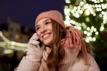 holidays, communication and people concept - portrait of beautiful happy young woman calling on smartphone at christmas tree in winter evening. happy woman calling on smartphone at christmas