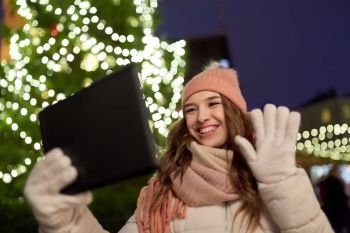 winter holidays and people concept - happy woman with tablet pc taking selfie or having video chat at christmas tree outdoors. woman with tablet pc at christmas tree outdoors