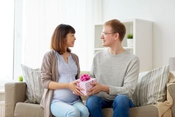 pregnancy, holidays and people concept - happy husband giving birthday present to his pregnant wife at home. husband giving birthday present to pregnant wife