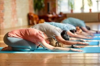 fitness, sport and healthy lifestyle concept - group of people with personal trainer doing yoga exercises on mats in gym or studio. group of people doing yoga exercises at studio